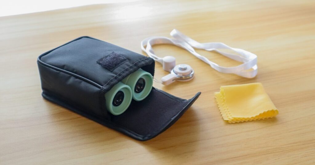 付属の専用ケースにネックストラップを付けたクロスロード双眼鏡を収納し、レンズクリーナーを並べた写真