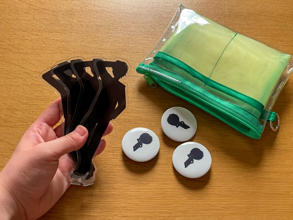 重ねたアクスタと缶バッジをまとめてポーチに入れようとしている様子